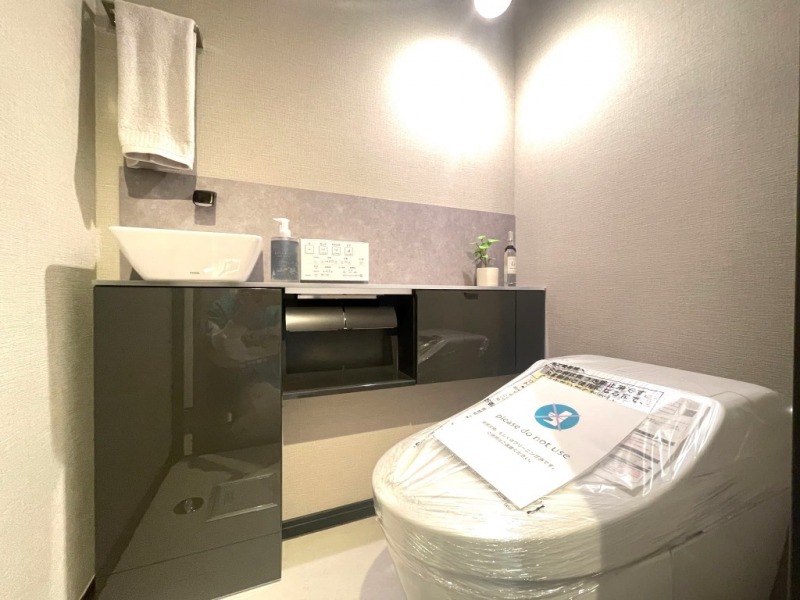 【トイレ】お手入れのしやすいタンクレスで、すっきりとしたデザインの温水洗浄機能付きトイレ。室内はシックな上質空間です。カウンター付きの便利な専用手洗いスペースも設けられています。