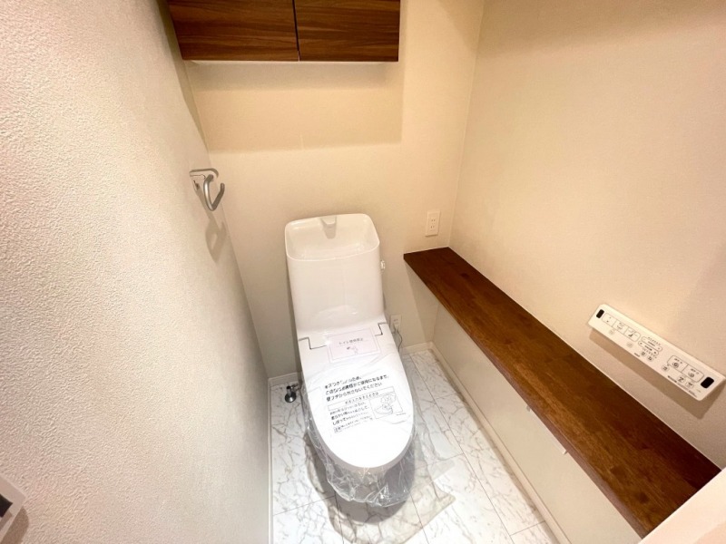 【トイレ】すっきりとしたデザインで清潔感があり、落ち着ける空間です。トイレもうれしい洗浄機能付きです。吊戸棚も設置されており、トイレットペーパーなどが収納できます。