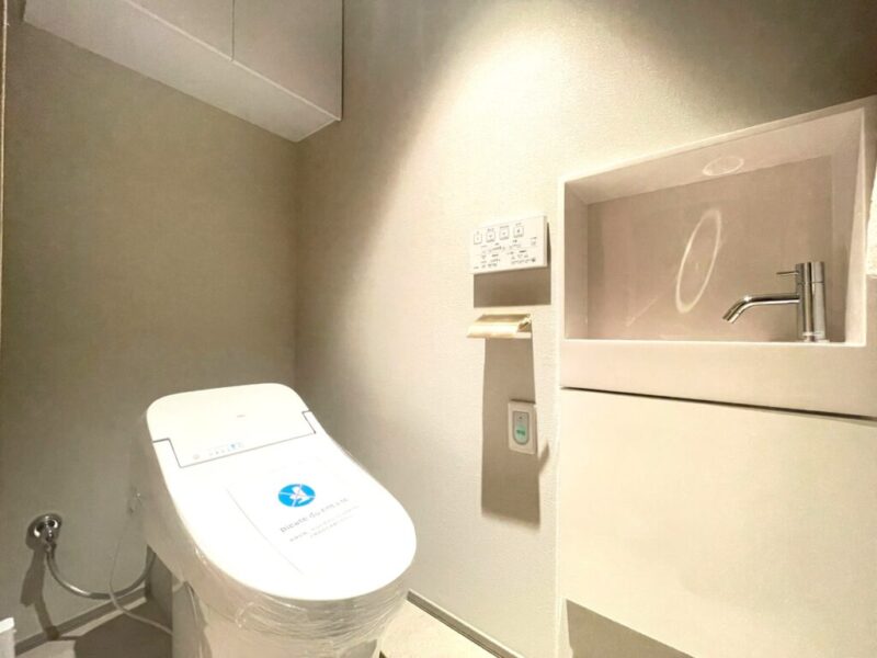 【トイレ】お手入れのしやすいタンクレスで、すっきりとしたデザインの温水洗浄機能付きトイレ。室内は清潔感があり落ち着く上質な空間です。トイレットペーパーなどが収納できる吊戸棚を備え、便利な専用手洗いスペースも設けられています。