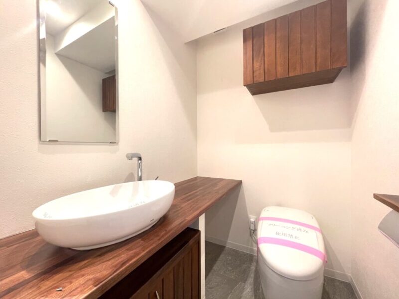 【トイレ】タンクレスですっきりとしたデザインのウォシュレット付きトイレです。室内は天然木の温もりを感じる落ち着いた上質な空間です。吊り戸棚やミラー付の便利な専用手洗いスペースが設けられています。