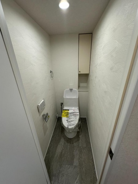 【トイレ】すっきりとしたデザインで清潔感があり、落ち着ける空間です。トイレもうれしい洗浄機能付きです。吊戸棚も設置されており、トイレットペーパーなどが収納できます。
