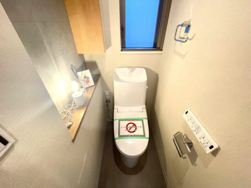 【トイレ】すっきりとしたデザインで清潔感があり、落ち着ける空間。トイレは温水洗浄機能付きです。吊戸棚も設置されており、トイレットペーパーなどが収納できます。トイレにも窓があり、こもりがちな臭いも換気ができて快適です。ちょっとした物が飾れるカウンターも付いています。