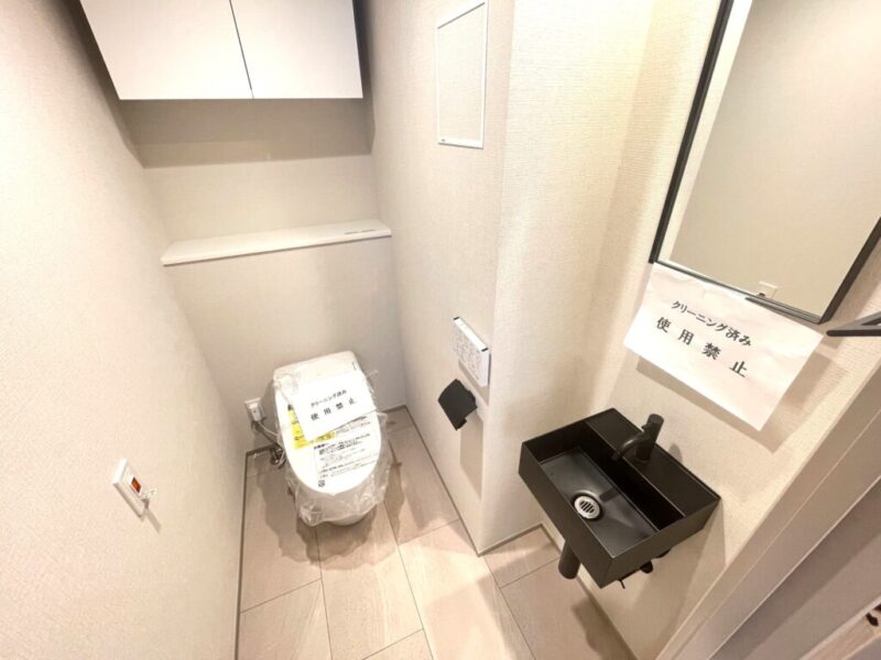 【トイレ】お手入れのしやすいタンクレスで、すっきりとしたデザインの温水洗浄機能付きトイレ。室内は清潔感があり落ち着く上質な空間です。トイレットペーパーなどが収納できる吊戸棚を備え、ミラー付きの便利な専用手洗いスペースも設けられています。