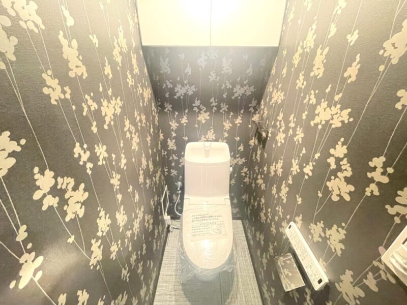 【トイレ】華やかさもありつつ、落ち着いた色味で纏まった空間です。トイレは温水洗浄機能付きです。吊戸棚も設置されており、トイレットペーパーなどが収納できます。