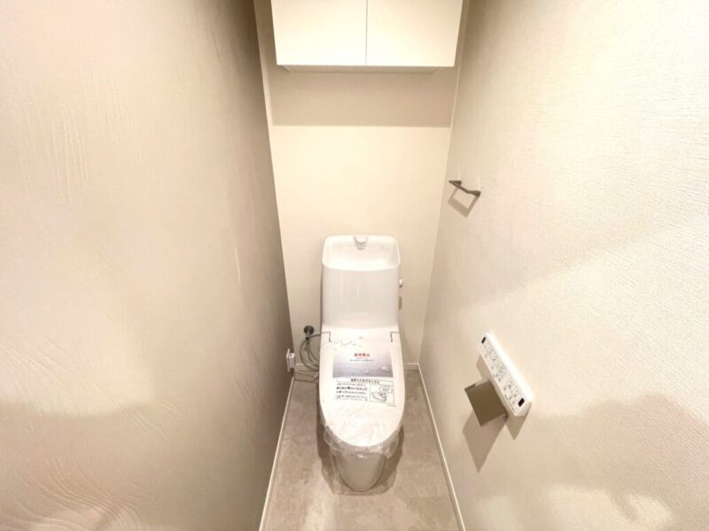 【トイレ】室内はホワイトを基調としていて清潔感があり、すっきりとした落ち着ける空間。トイレは温水洗浄機能付きです。吊戸棚も設置されており、トイレットペーパーなどが収納できます。