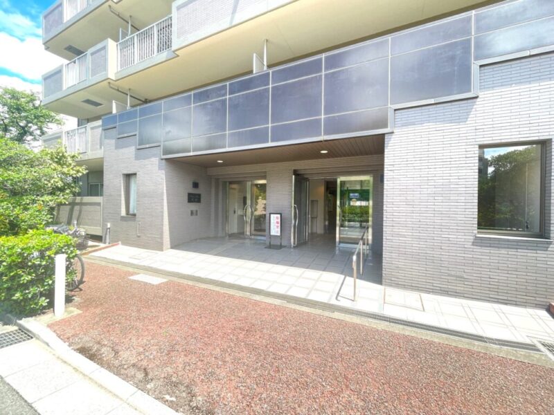 【エントランス】植栽に囲まれたエントランスは、落ち着きと品格を感じさせる佇まい。住まいへ帰るたびに穏やかな気持ちを演出します。オートロック、防犯カメラ、宅配ボックスなど、日々の暮らしを支える設備を採用。管理員の日勤管理も安心感につながります。