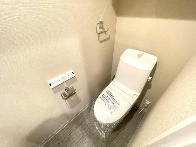 【トイレ】室内はホワイトを基調としていて清潔感があり、すっきりとした落ち着ける空間。トイレは温水洗浄機能付きです。吊戸棚も設置されており、トイレットペーパーなどが収納できます。