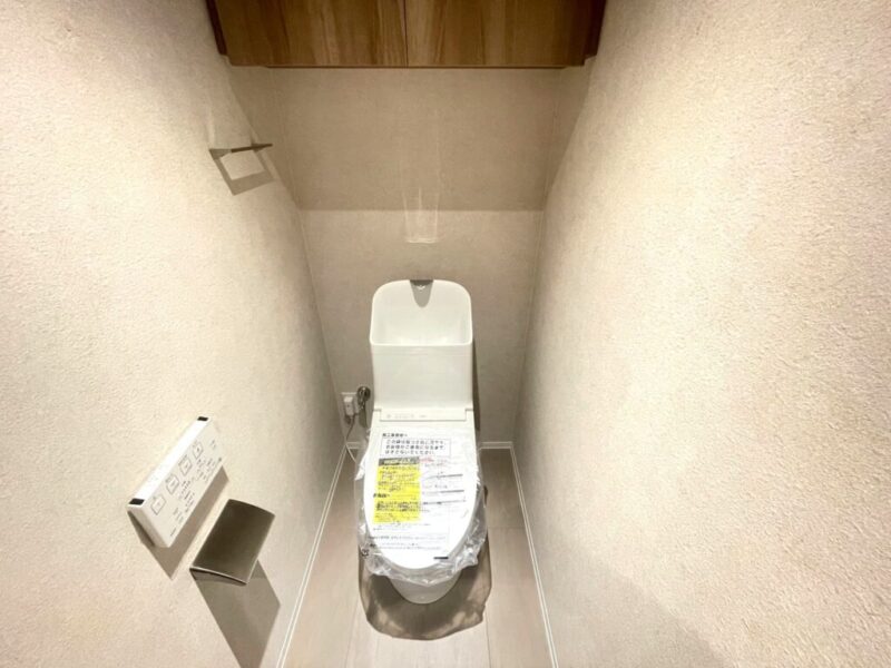 【トイレ】室内は優しい色合いで纏まり清潔感のある、すっきりとした落ち着いた空間。トイレは温水洗浄機能付きです。吊戸棚も設置されており、トイレットペーパーなどが収納できます。