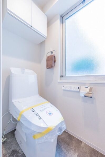 【トイレ】すっきりとしたデザインで清潔感があり、窓付きで明るく落ち着ける空間。トイレは温水洗浄機能付きです。吊戸棚も設置されており、トイレットペーパーなどが収納できます。