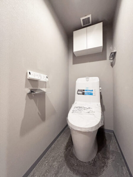 【トイレ】すっきりとしたデザインで清潔感があり、落ち着ける空間。トイレは温水洗浄機能付きです。吊戸棚も設置されており、トイレットペーパーなどが収納できます。