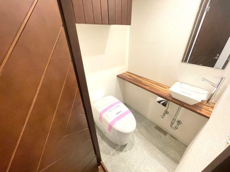 【トイレ】タンクレスですっきりとしたデザインのウォシュレット付きトイレ。室内は天然木の温もりを感じる落ち着いた上質な空間です。吊り戸棚が設置され、消耗品も収納できます。カウンターとミラー付の便利な専用手洗いスペースが設けられています。