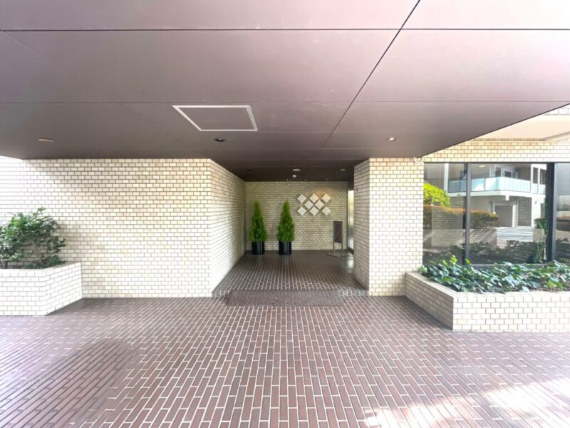 【エントランス】植栽に囲まれた落ち着いたタイル敷の上品なアプローチ。オートロックや防犯カメラを備え、安心感に配慮されたセキュリティ体制です。