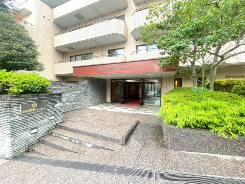 【エントランス】周囲の緑に馴染む落ち着いた色調でまとめられたエントランスが、住まいへの品格あるアプローチを演出します。駅近でありながら穏やかな邸宅感を感じさせる佇まいです。オートロックを採用し、防犯カメラも設置された安心感のあるセキュリティ環境です。管理員による管理体制も整えられ、日々の暮らしを支えます。宅配ボックスも備えているため、不在時の荷物の受け取りにも便利です。