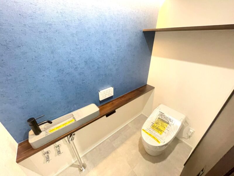 【トイレ】お手入れのしやすいタンクレスのすっきりとしたデザインの温水洗浄機能付きトイレ。室内は清潔感があり落ち着く上質な空間です。トイレットペーパーなどが収納できる吊棚を備え、カウンター付きの便利な専用手洗いスペースも設けられています。