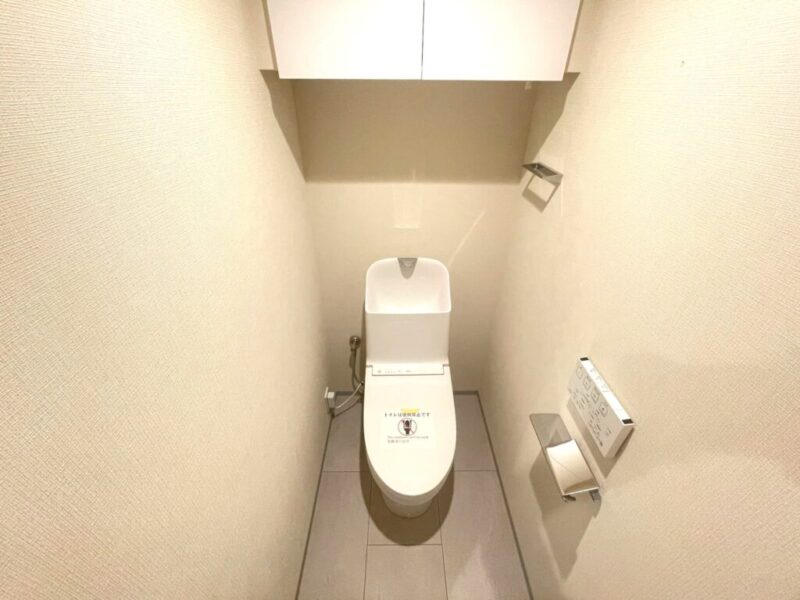 【トイレ】すっきりとしたデザインで清潔感があり、落ち着ける空間。トイレは温水洗浄機能付きです。吊戸棚も設置されており、トイレットペーパーなどが収納できます。