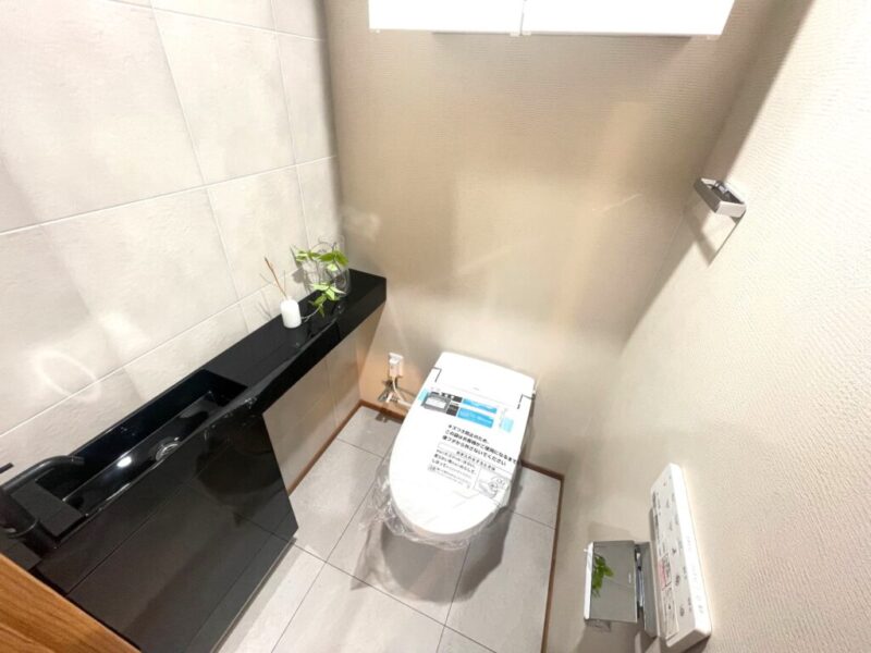 【トイレ】お手入れのしやすいタンクレスのすっきりとしたデザインの温水洗浄機能付きトイレ。室内は清潔感があり落ち着く上質な空間です。トイレットペーパーなどが収納できる吊戸棚を備え、シックなカウンター付きの便利な専用手洗いスペースも設けられています。