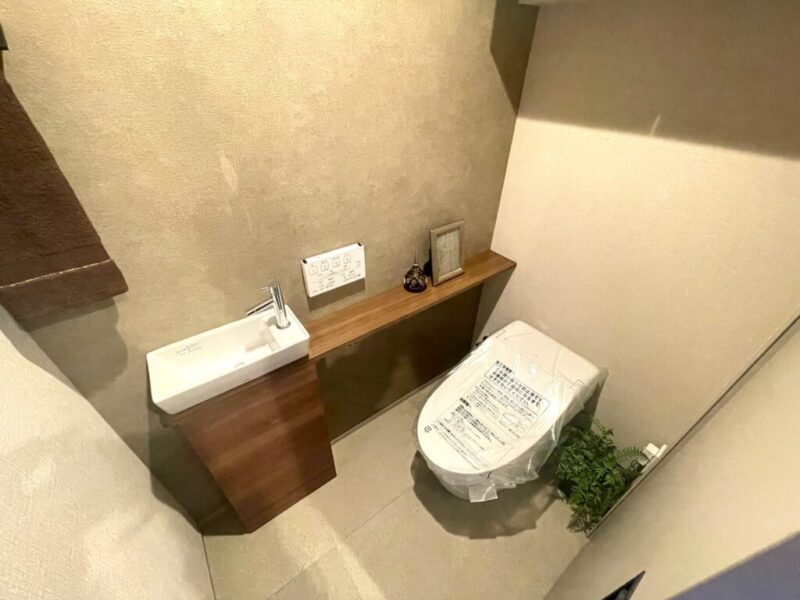 【トイレ】お手入れのしやすいタンクレスのすっきりとしたデザインの温水洗浄機能付きトイレ。室内は清潔感があり落ち着く上質な空間です。トイレットペーパーなどが収納できる吊戸棚を備え、カウンター付きの便利な専用手洗いスペースも設けられています。