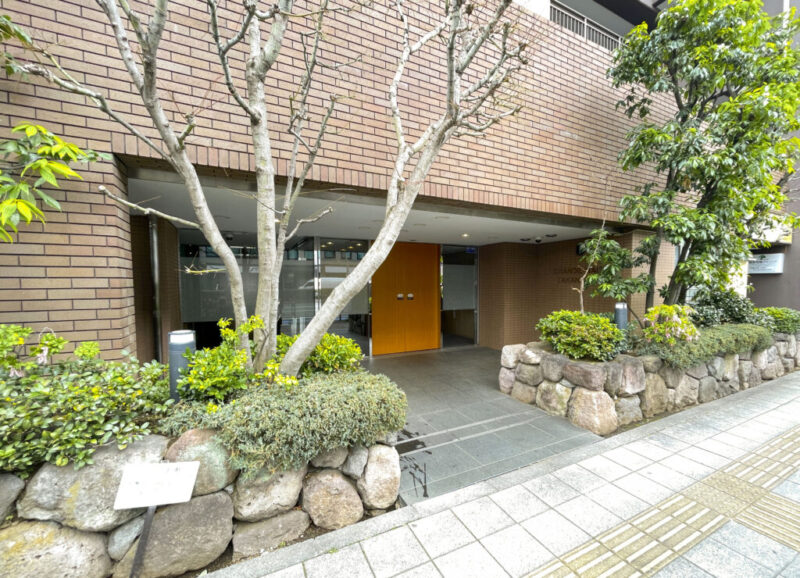 【エントランス】高輪の街並みに調和する、落ち着いた雰囲気のエントランスが住まう方を迎えます。植栽や素材の質感にも配慮されたアプローチが、日々の帰宅に心地よさを添え、住まいとしての品格を感じさせます。オートロックや防犯カメラを備え、住まう方の安心に配慮したセキュリティ体制です。さらに宅配ボックスも設置されており、不在時の荷物の受け取りにも便利。防犯性と日々の暮らしやすさを両立しています。